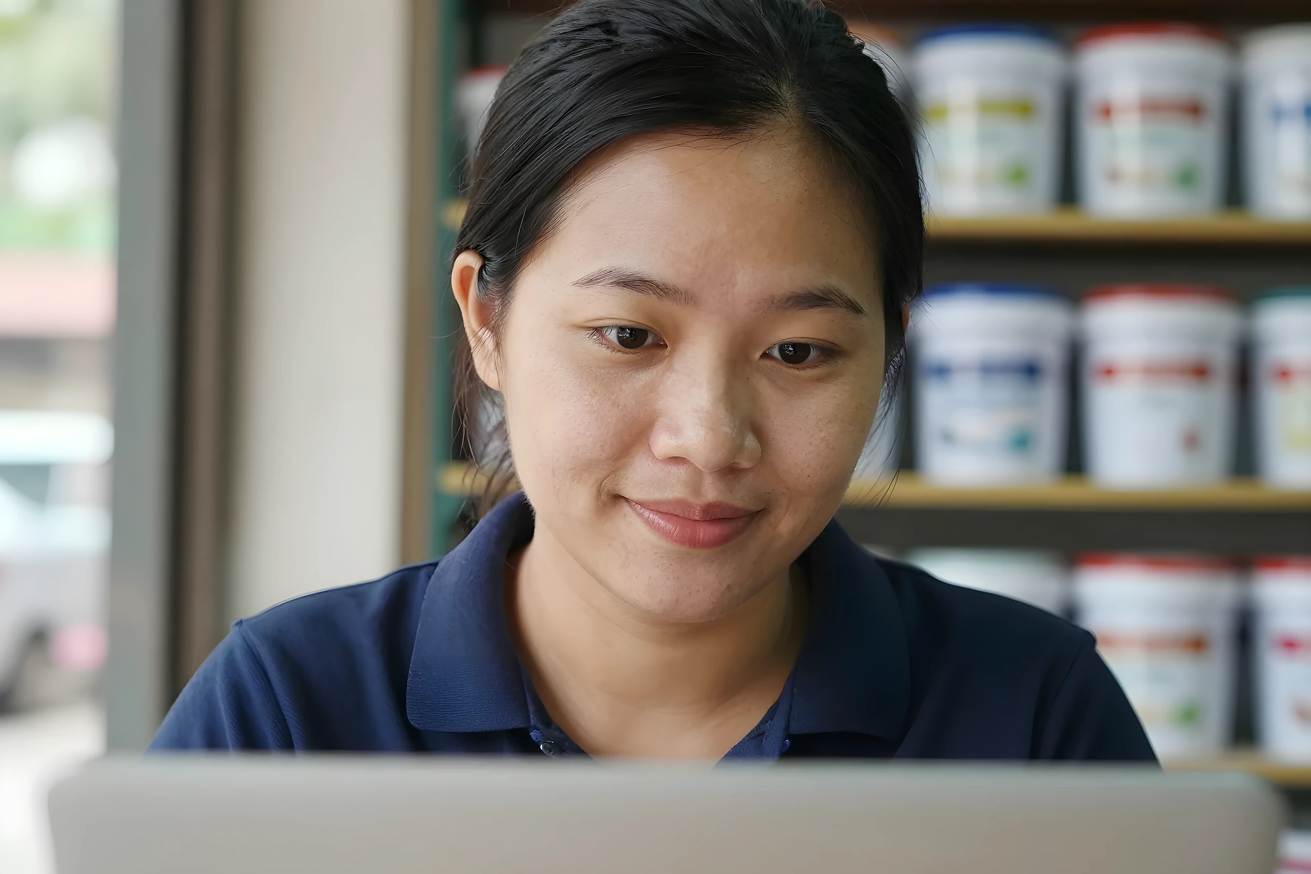 Nữ chủ cửa hàng sơn mỉm cười nhìn laptop cập nhật giá trên website vật liệu